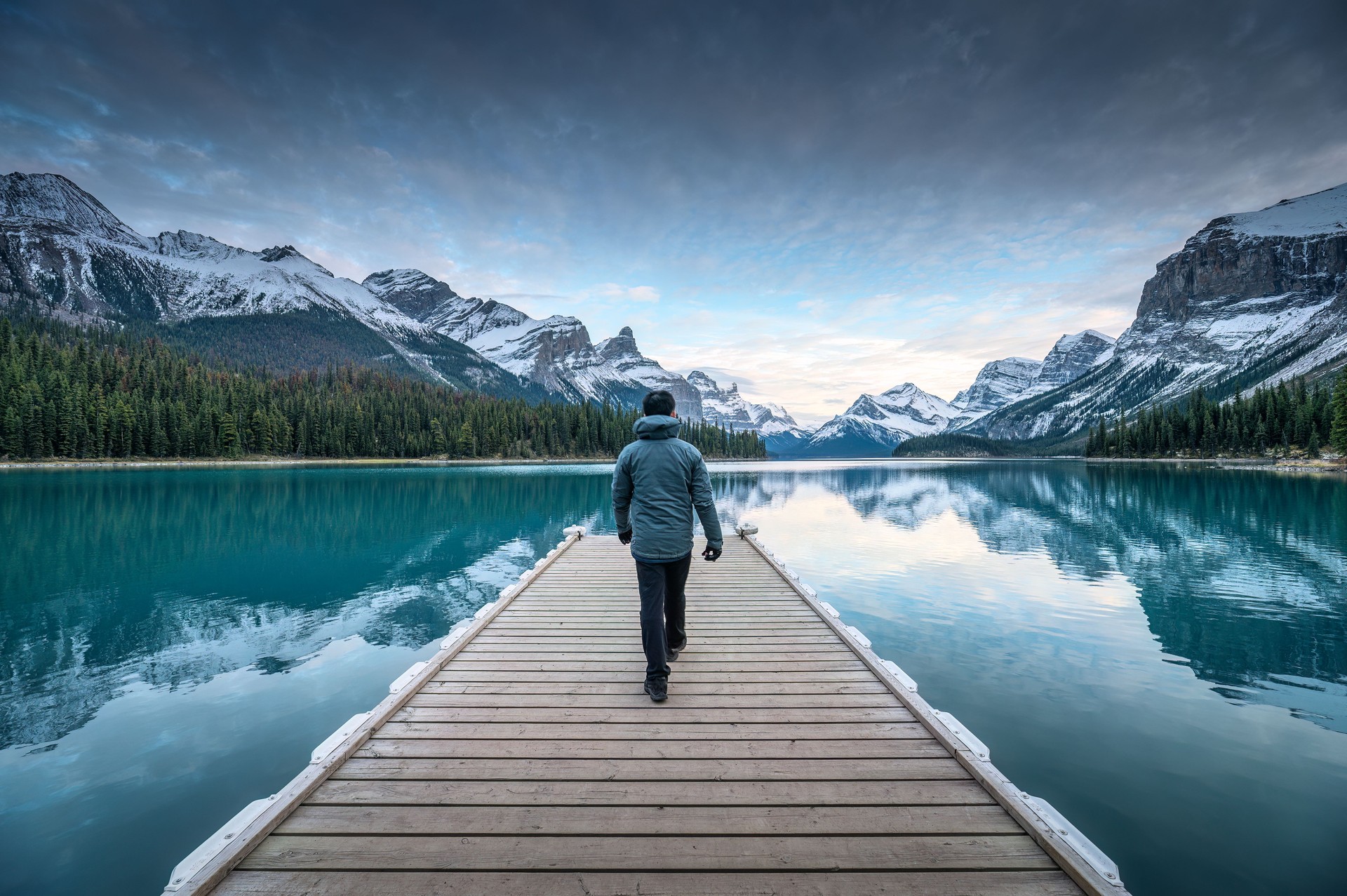 Male tourist walking on wooden pier among world famous iconic Spirit Island on Maligne Lake at Jasper national park